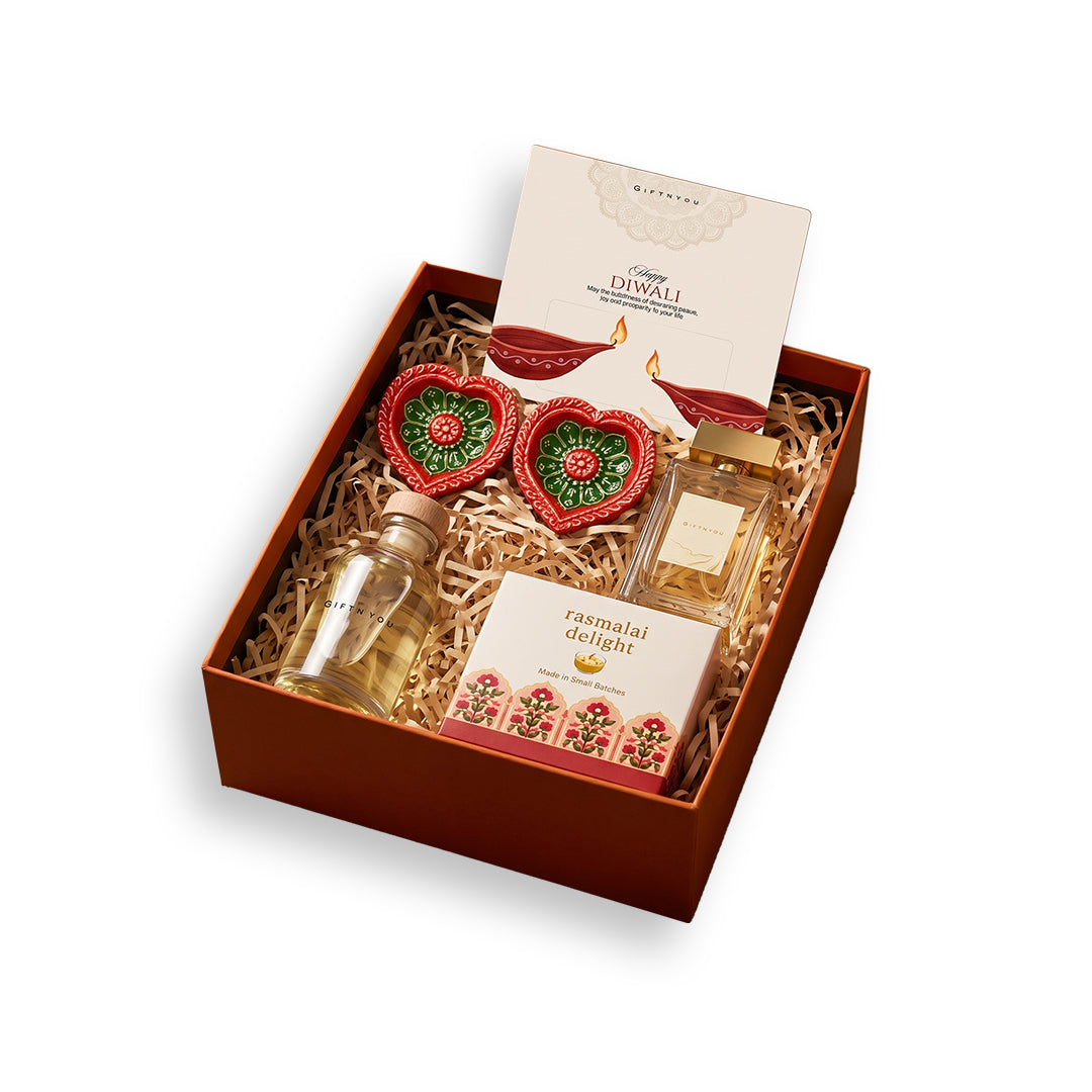 GiftNYou Diwali hamper with perfume, Rasmalai Delight candle, two diyas, stoppered bottle and card on white