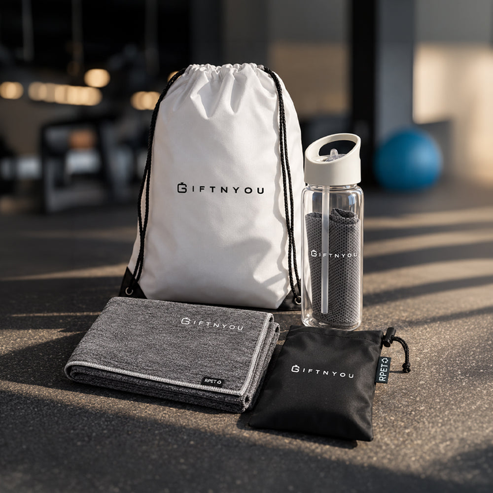 The Active Refresh Kit by GiftNYou with clear bottle with carry handle and grey towel inside, additional grey sports towel, black drawstring storage pouch in a fitness setting